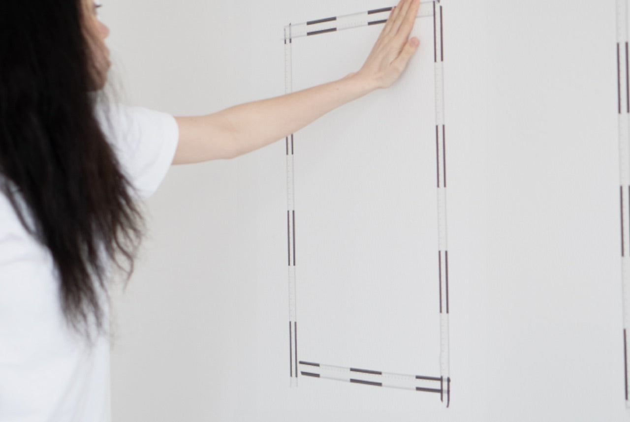 Frau klebt ein Viereck mit Klemab an die Wand